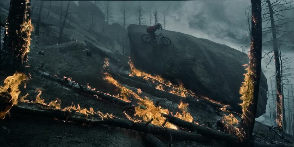 A mountain biker hitting a big wall ride on rock through a burning forest