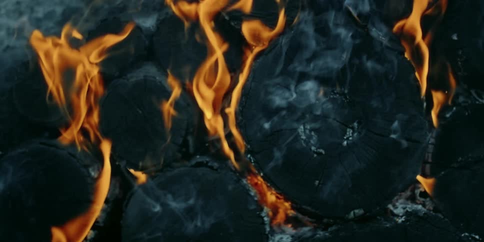 Charred burning wood in flames and smoke is rising
