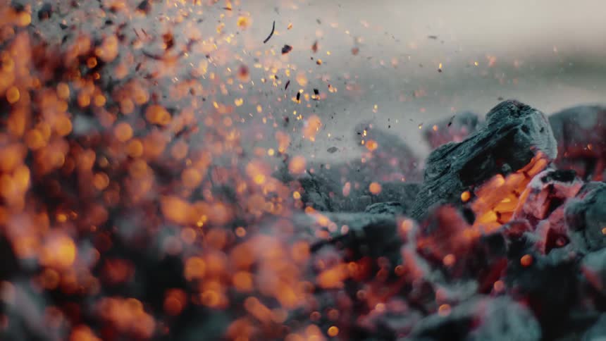 Smoke and embers rise from burning charred wood
