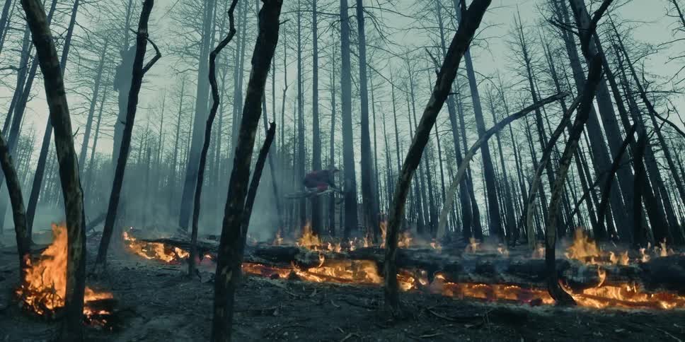 A person wearing a helmet jumps a mountain bike through a smokey forest fire