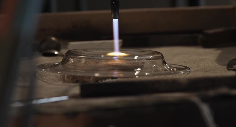 A person uses a torch to heat a glass plate