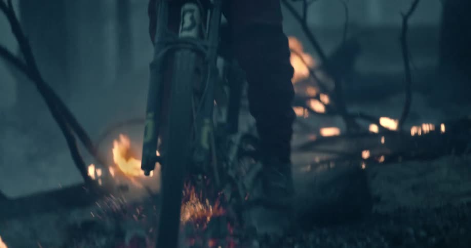Person on bicycle jumps over burning fire in fog covered woods