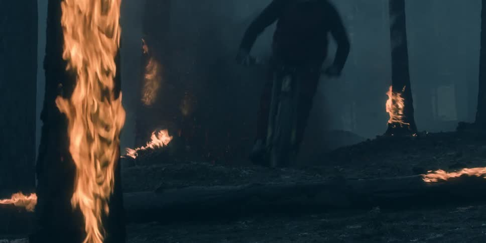 A person on a mountain bike rides through a burning forest with trees in flames