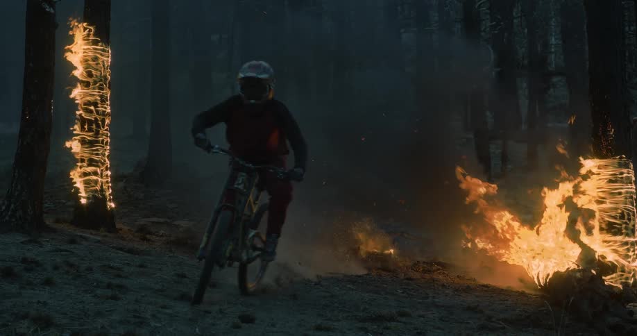 A person rides a mountain bike out of smoke in a burning forest with trees in flames