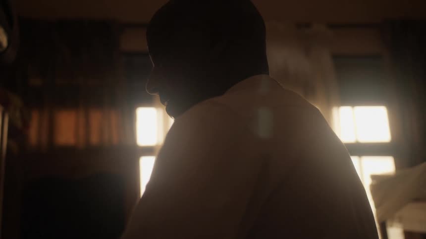 A man dressing with a white shirt inside a dimly lit room