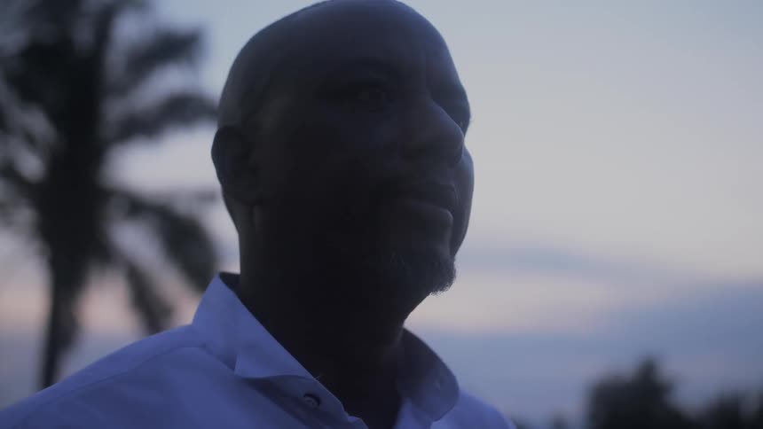 Man standing outside staring off into the distance with a slight smile on his face at sunset
