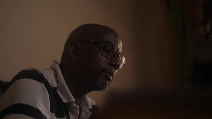 A man is sitting in a room and is wearing glasses