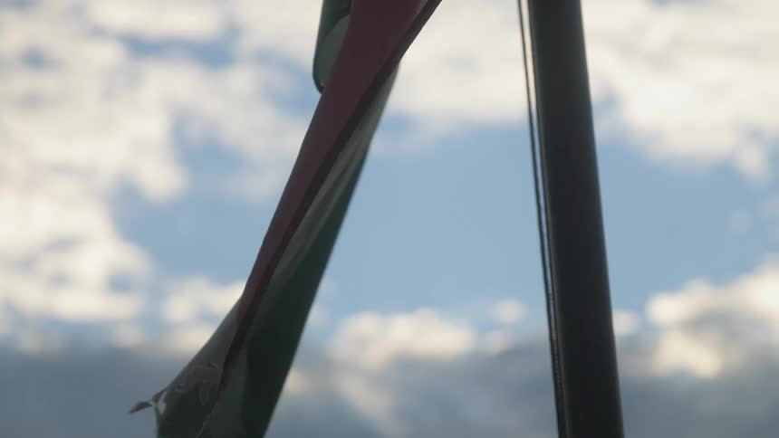 A frayed flag in a flagpole waving slowly in the wind