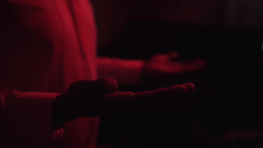 A man inside a room bathed in red light lifts his hands palms up