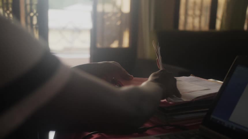 A person picks up a folder from a pile of papers over a desk at home