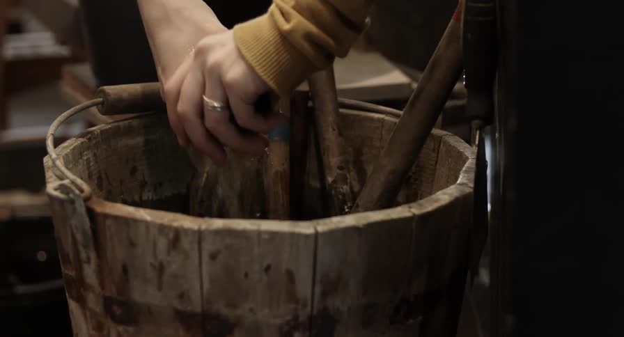 A rag is dipped and the water in a wood bucket filled with tools and then wrung out