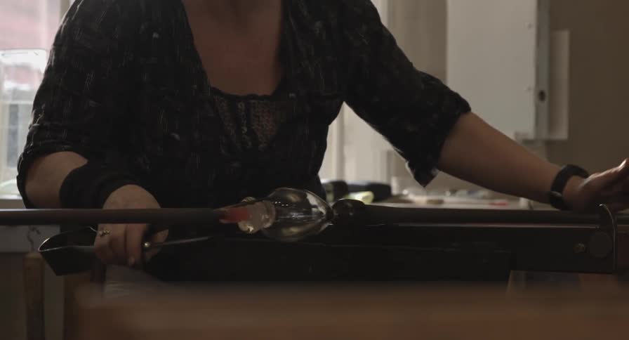 A woman rolls a metal rod back and forth with a glass attached