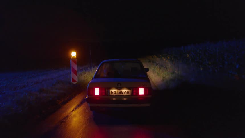 A vehicle drives down a single lane road and past a flashing red light at night