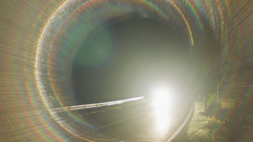 Car headlights brighten road and trees as car drives along curve