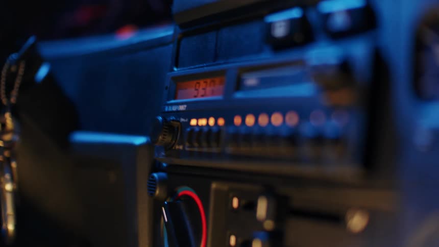A hand turns on the radio in the dashboard of a moving car