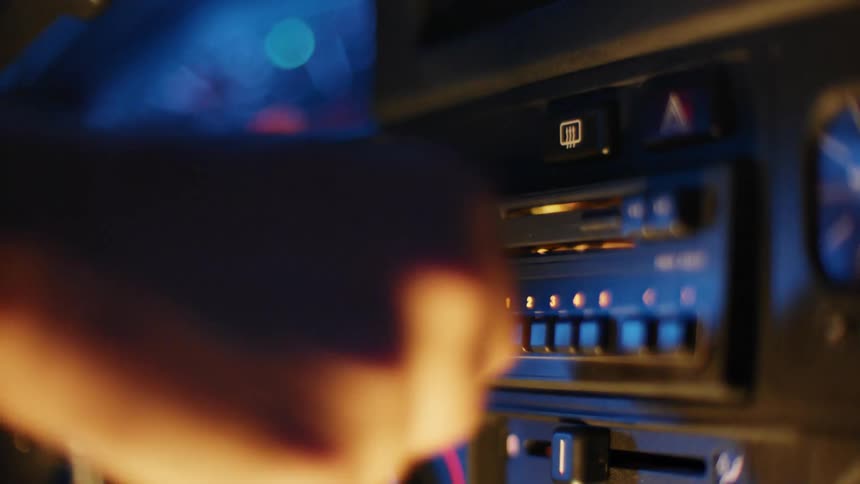 A man puts a cassette on the radio in the dashboard of a car