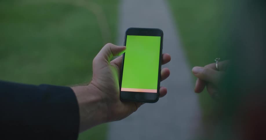 A person holds a cell phone with a green screen and scrolls on it
