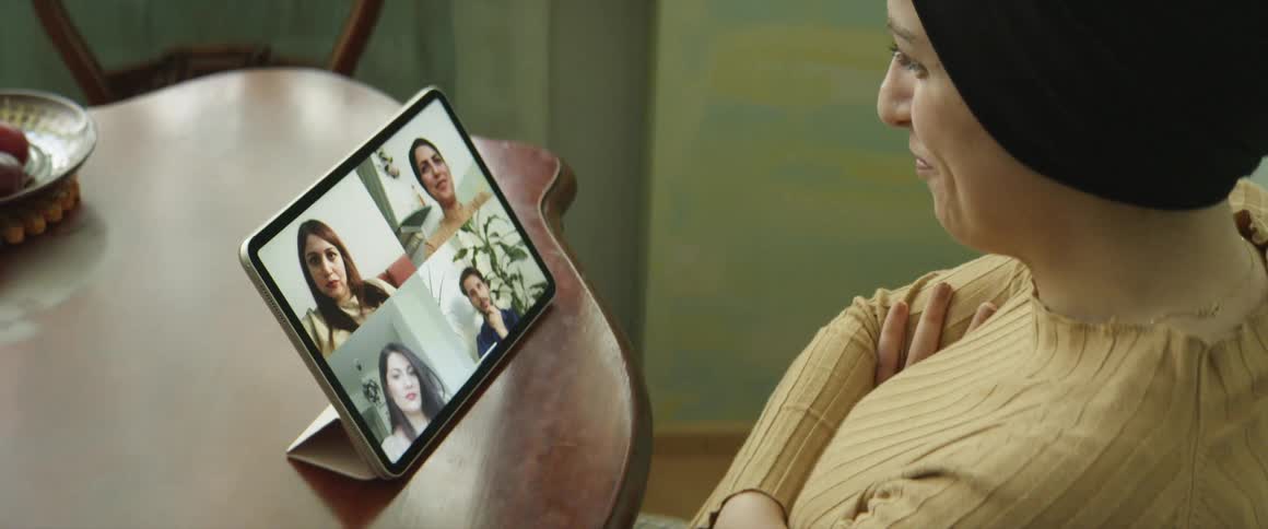 A woman sitting on a chair at a table video chatting on a tablet