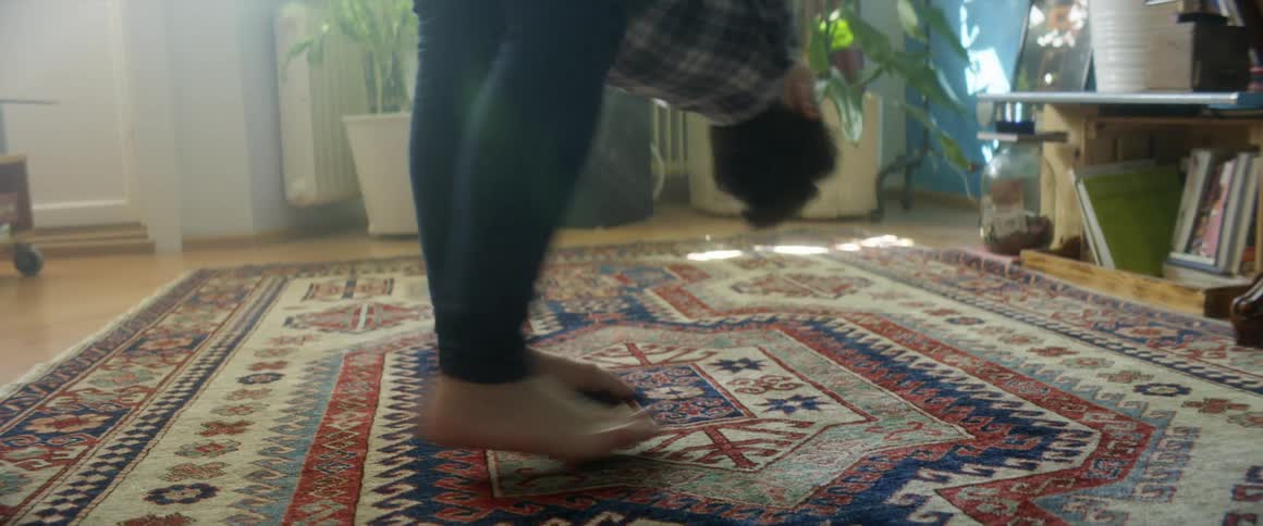 A parent plays with their son spinning him around upside down then flipping him around so he stands on the floor the are on a multicolored rug