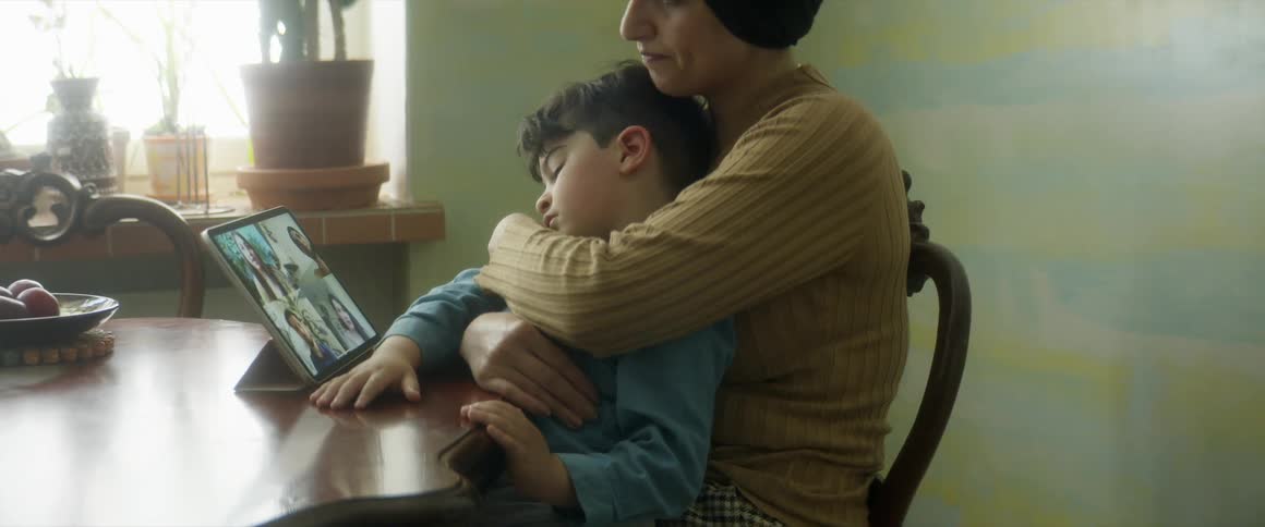 A woman sitting in a chair at a table holding a boy using a tablet