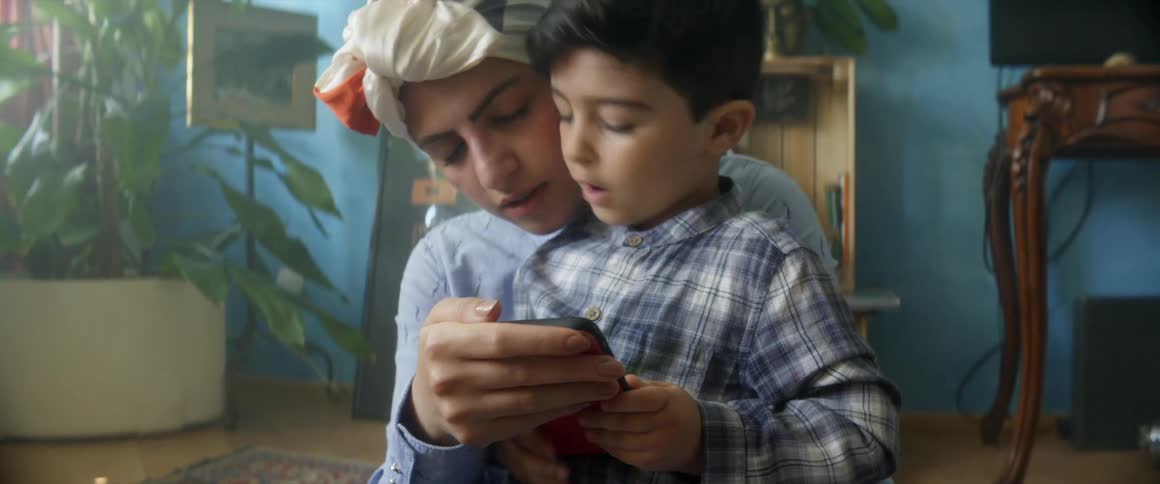 A woman holds her toddler son tightly as they look at a cell phone together