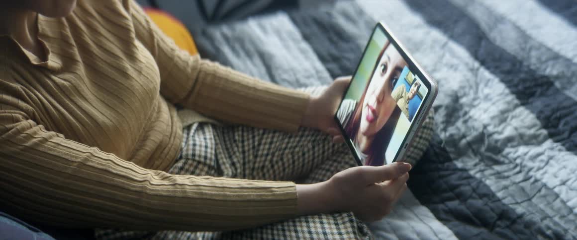 A woman sitting on a bed with pillows holding a tablet
