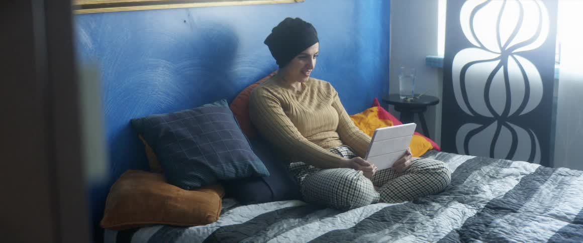 A young woman sitting in her bedroom talks with someone on a tablet