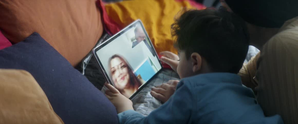 A young boy lays in front of a tablet having a video call