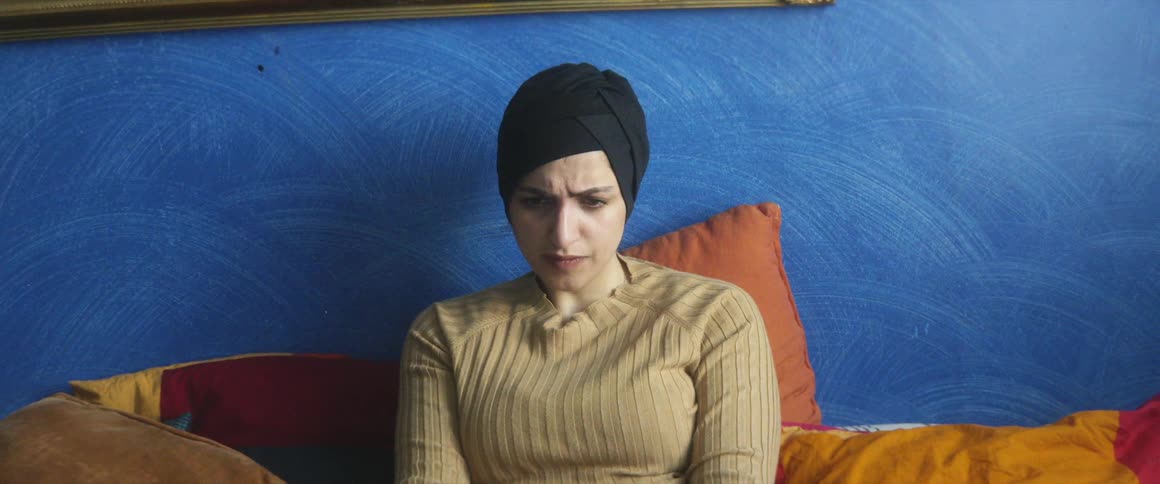 A woman video chats on her laptop while sitting on her bed