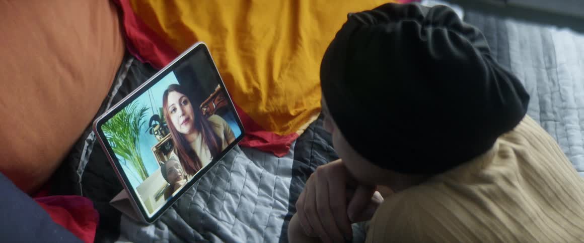 A woman laying in bed is in a video call with a friend on a tablet