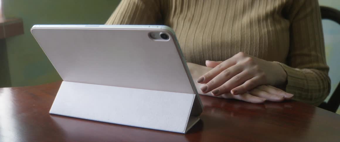 A woman sitting at a table looks at a tablet on a stand on the tables surface