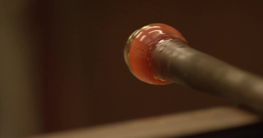 A roller shapes a small piece of liquid glass