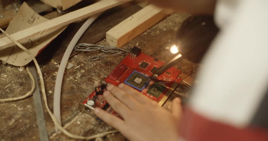 A teenager uses a soldering gun on a circuit board in his garage