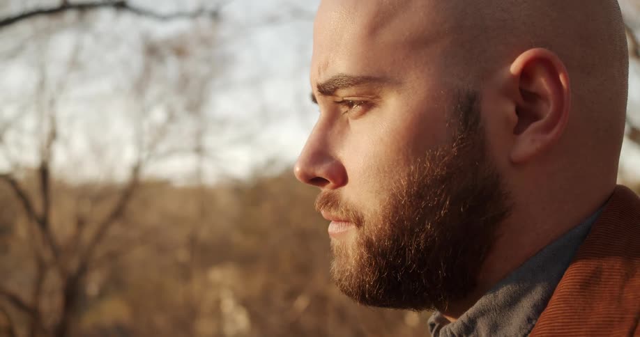 A man looking off into the distance with trees plants the sky and clouds in the background