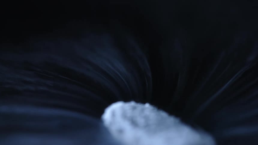 Piece of dry ice spinning on a black surface leaving a swirling trace of white smoke