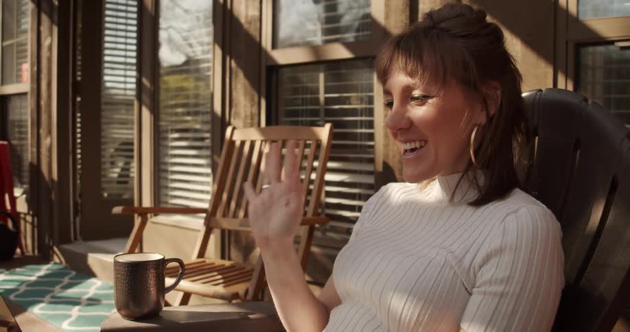 Woman sitting on porch smiles as she waves