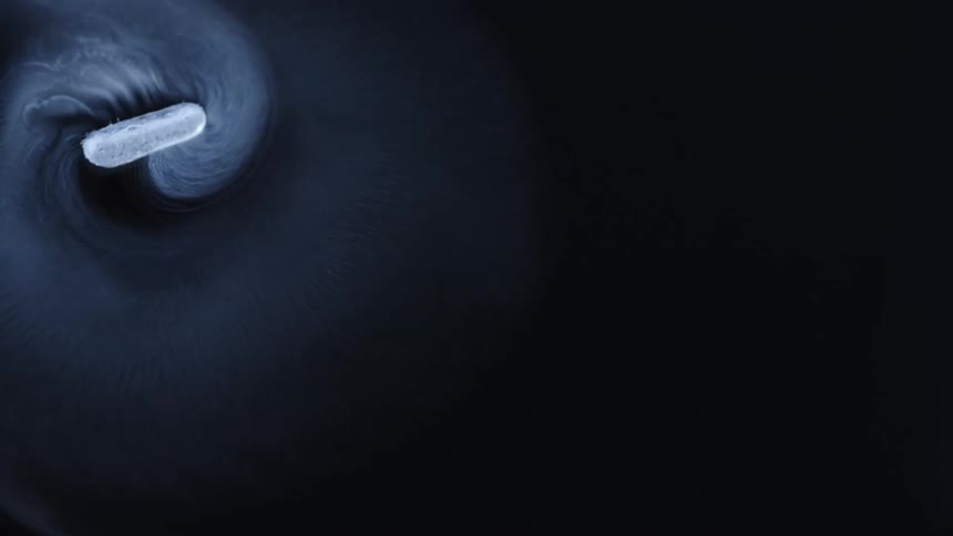 An ice cube spins in a circle through dark blue gray liquid
