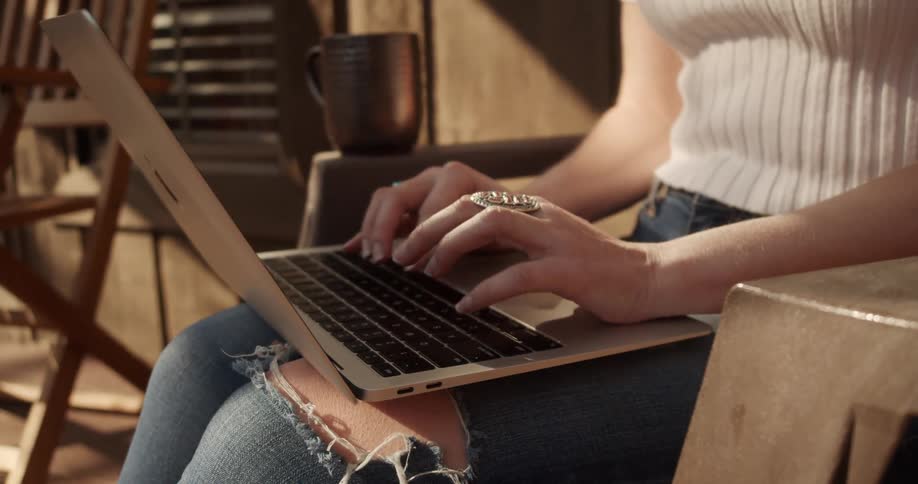 Man sitting outdoors types on the keyboard of a laptop over her lap