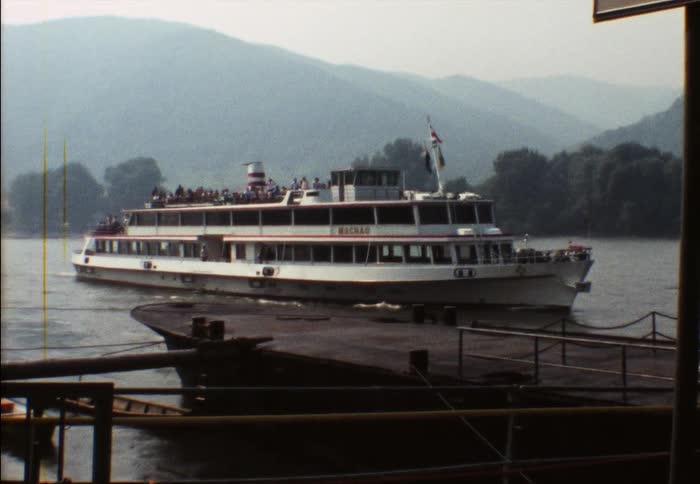 People crowd ship arriving at dock with fog obscuring mountains in background