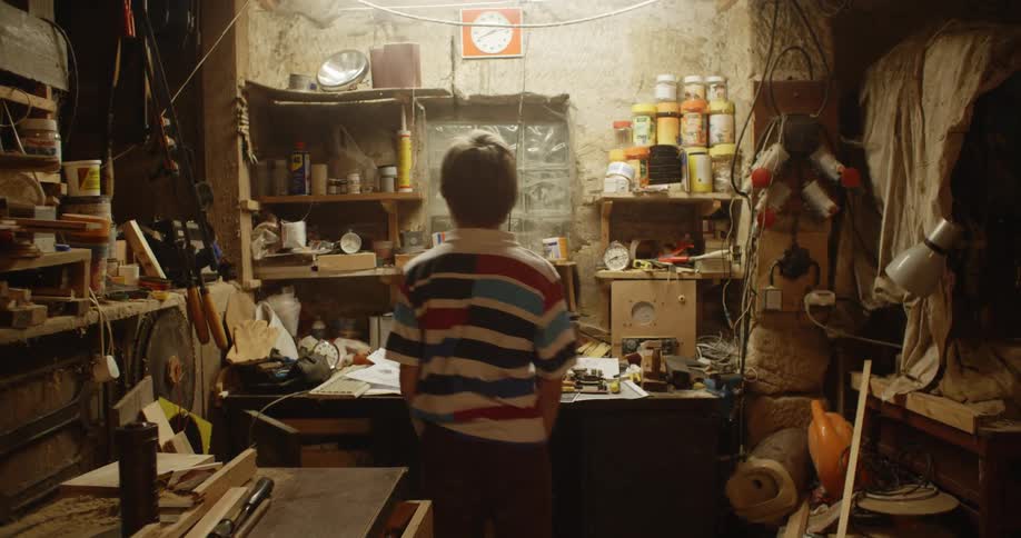 Young blonde boy playing in the basemant places something on a shelf in the wall