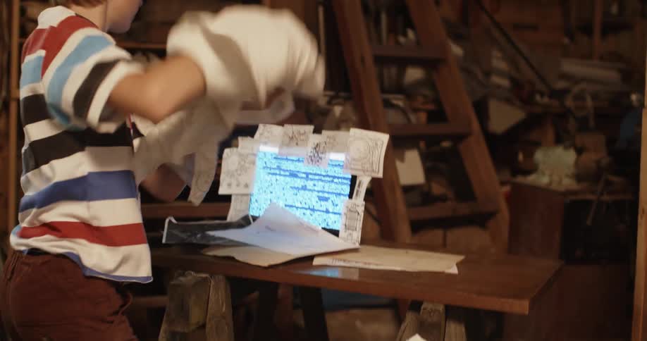 Young boy reveals a laptop covered with paper notes over a table inside the basement