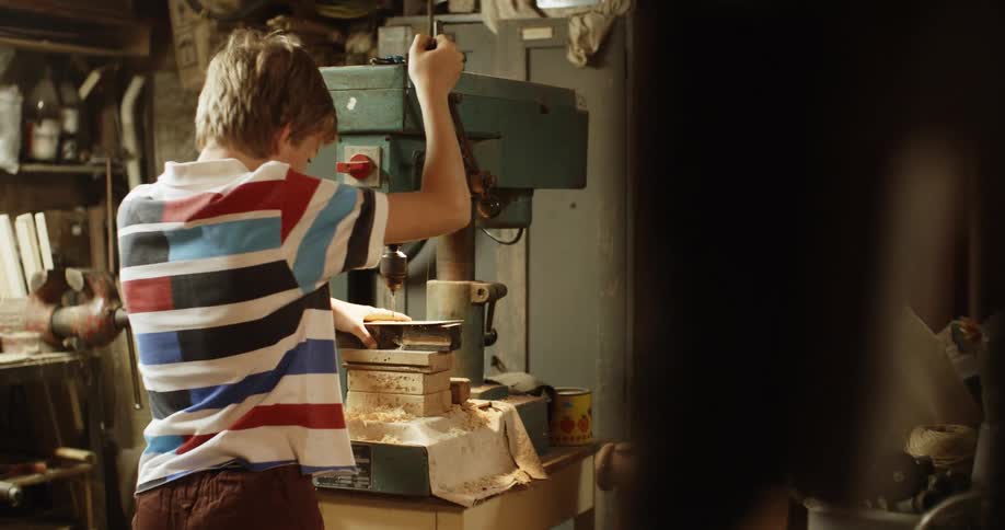 A boy is drilling with a machine into pieces of wood
