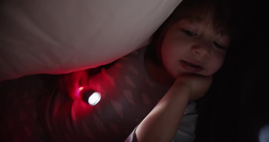 A small girl waves a flashes as she lies under a blanket in her pajamas