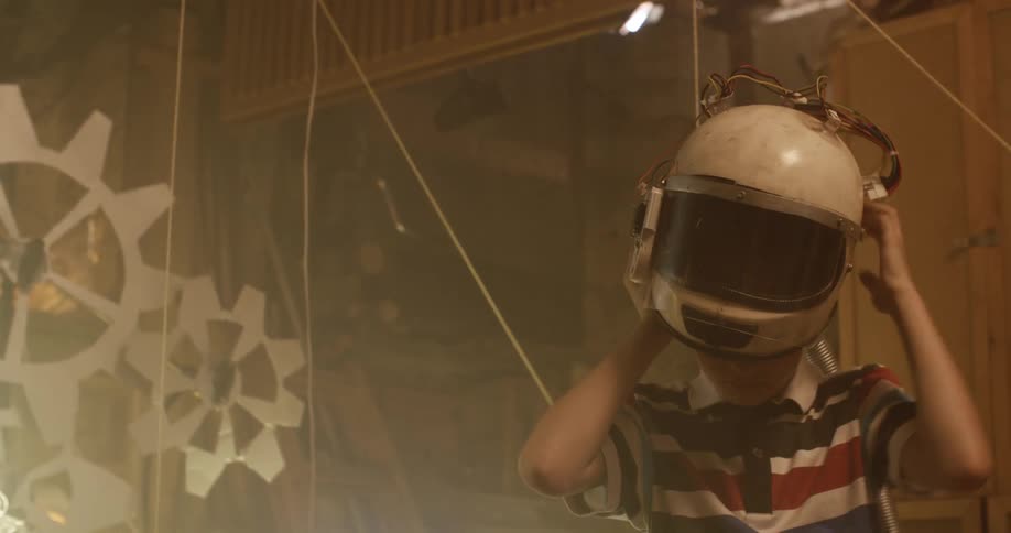 A boy puts on a helmet with wires connected to a nearby computer in his attic