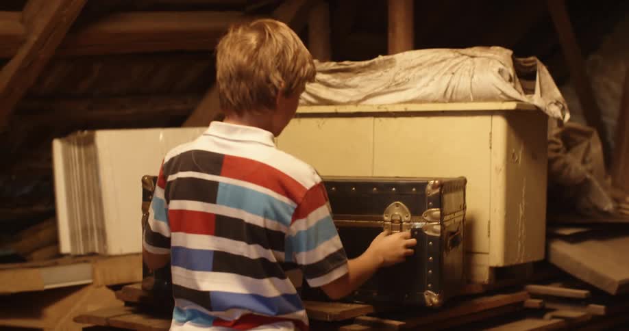 Yougn boy playing in the attic opens a chest filled with bright white light