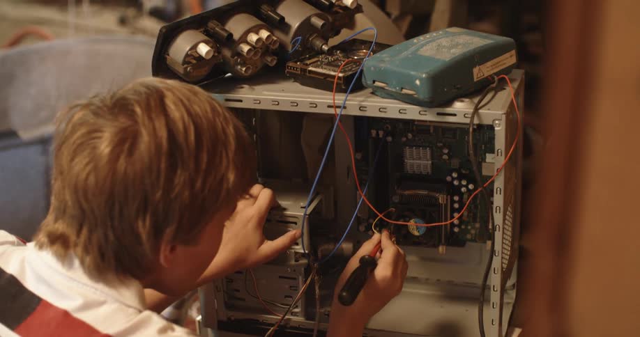 A boy in a workshop fixing a computer with a screwdriver with a hard drive on top