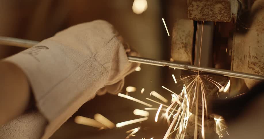 Sparks fly as a long thin piece of metal is held against a grinder