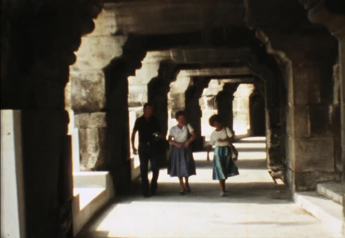 Three people walk together and talk under the stone arches