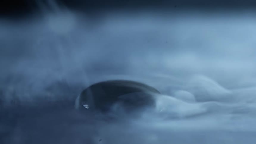 Liquid nitrogen fog flows and clears revealing a black droplet reflecting light