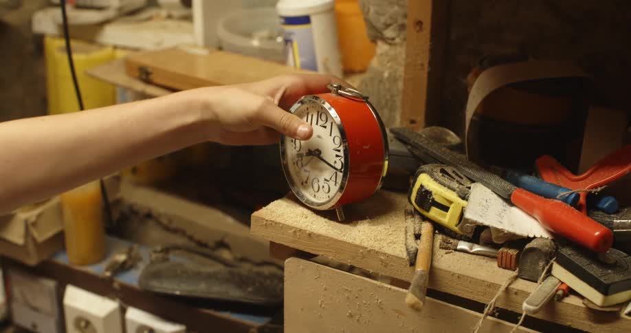 A person places a table clock on a surface covered in tools and sawdust
